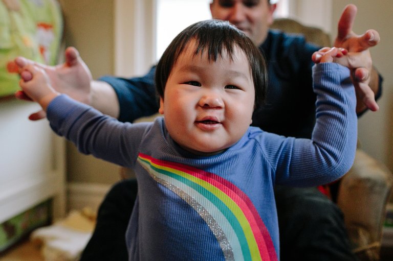 Father holds little boys hands helping him learn how to walk.