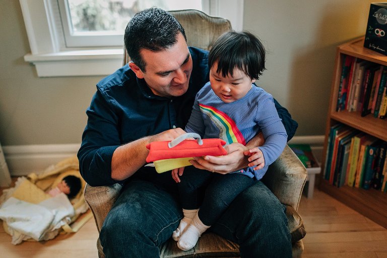 Little boy sits on fathers lap as father shows him a toy.