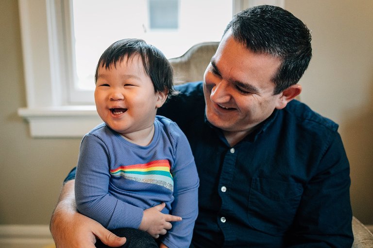 Little boy sits laughing on fathers lap.