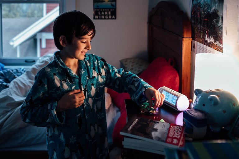Boy wearing pajamas standing in bedroom playing with toys on bedside table.