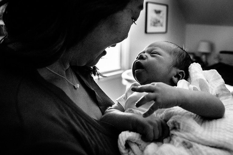 Black and white. Mother holds and looks at sleepy newborn baby.