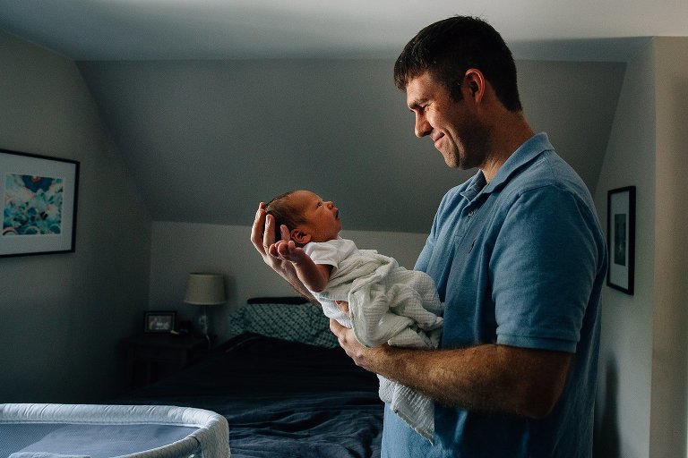 Father holds up and looks at newborn baby boy.