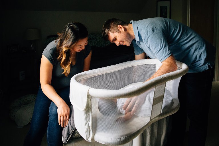Mother and father look at newborn baby sleeping in bassinet.