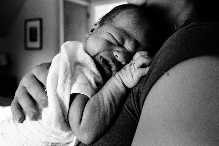 Black and white. Mother holds newborn baby boy as he scrunches up his little face.