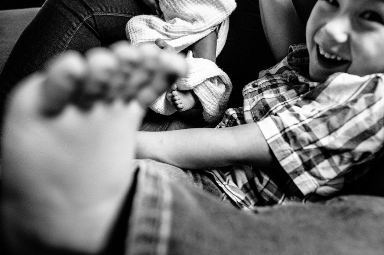 Black and white. little boy sitting on couch with his foot up it the air.