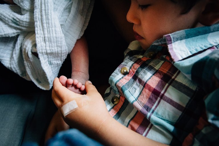 Young boy holds little brothers foot looking at his tiny toes.