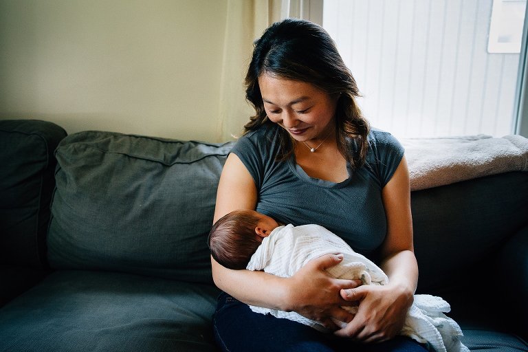 Mother sitting on couch breast feeding newborn baby.