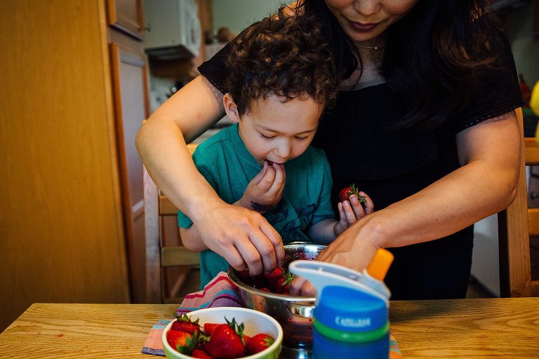 Mother with her arms around son as they wash and eat fresh strawberries.