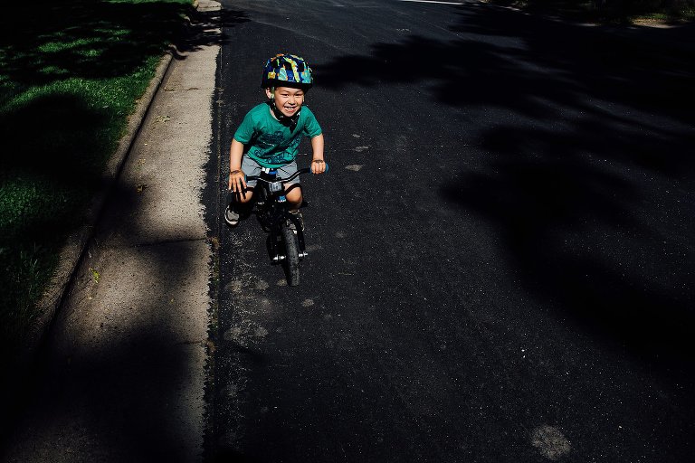Young boy rides his bike down the street with a big smile on his face.