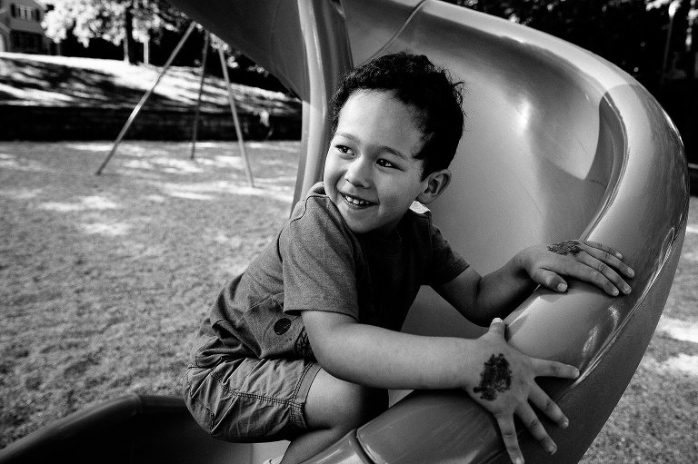 Black and white. Young boy going down a curvy slide at a park playground.