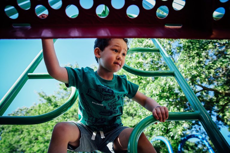 Young boy climbing up park play set reaching across to the platform.