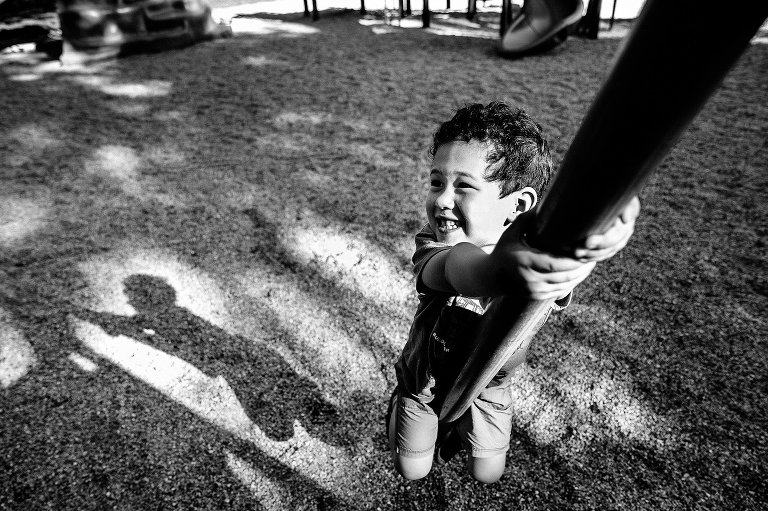 Black and white. Young boy climbs up pole while playing at a park playground.