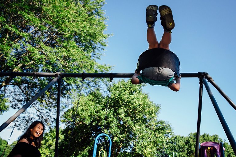 Expecting mother watches her son swing on a swing set at a park.