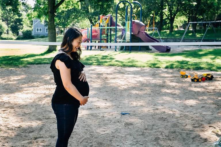 Maternity shot at a park. Expecting mother stands in the sand holding her belly at a park.