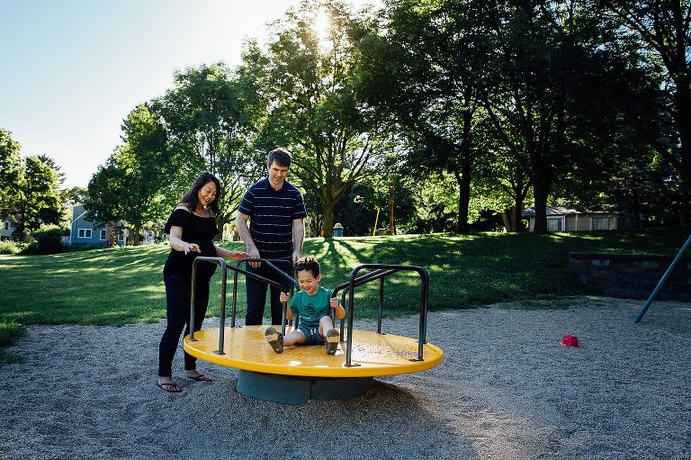 Family evening at the park. Father and pregnant mother play with their young son at a park at evening time.