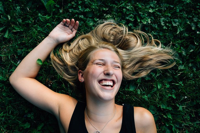 madison senior girl smiles on the grass with hair blown behind her