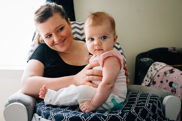 infant daughter is held upright by her mother. child makes eye contact with camera. 