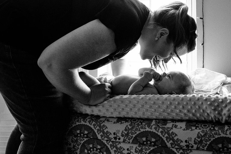 black and white. mother leans over infant daughter,side view, and they smile and laugh with each other. 