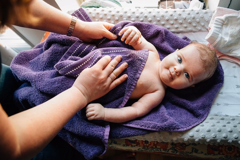 Infant swaddled in a purple towel makes eyes contact and smiles. Mother gently dries. 