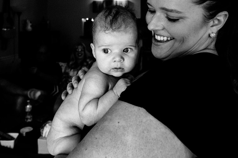 Mother smiles at infant, as infant looks toward a window. Black and white. 