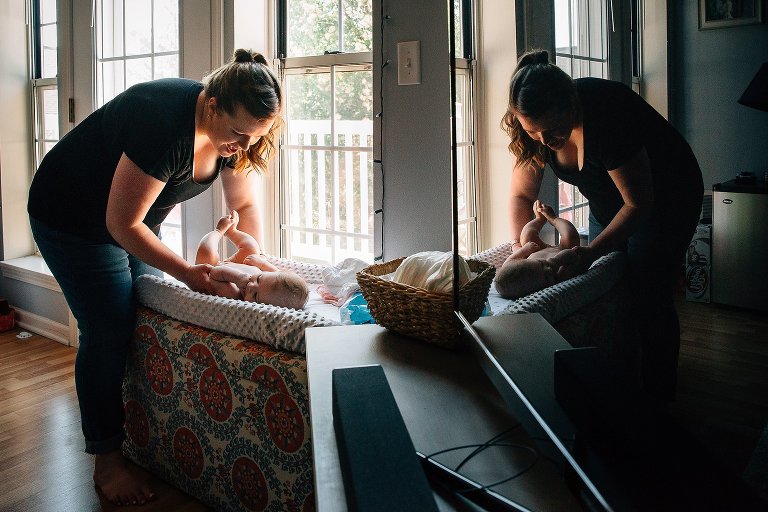 Mother picks up infant daughter. Their reflection is in the TV. 