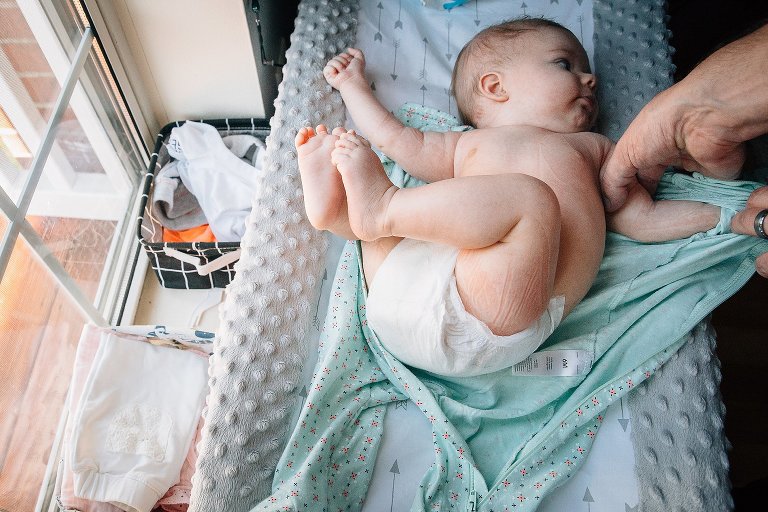 Father undresses infant daughter for a bath on her changing table. Her skin is wrinkled from her clothes. 