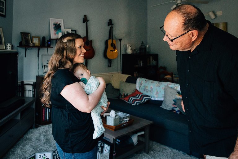 Grandfather checks on granddaughter, who is being held by mother as she tries to take a nap. 