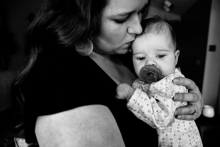 Black and white. Mother kisses infant daughter on head while child sucks on a pacifier. 