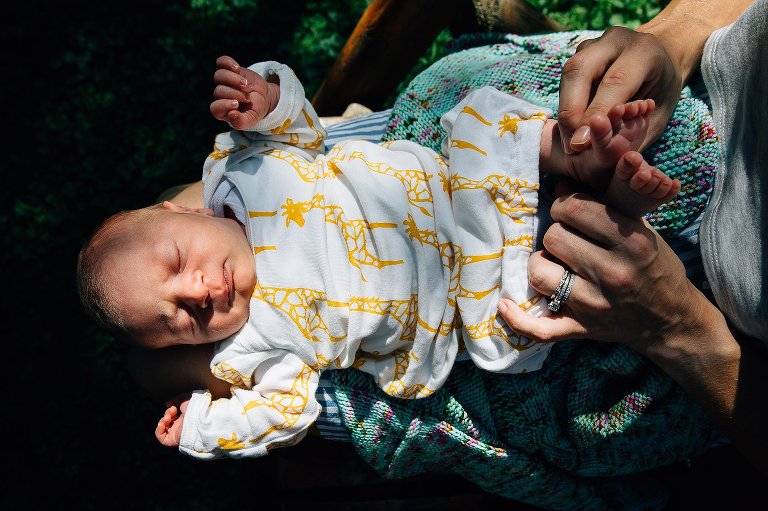 Newborn baby sleeping on moms lap outside in the sun.