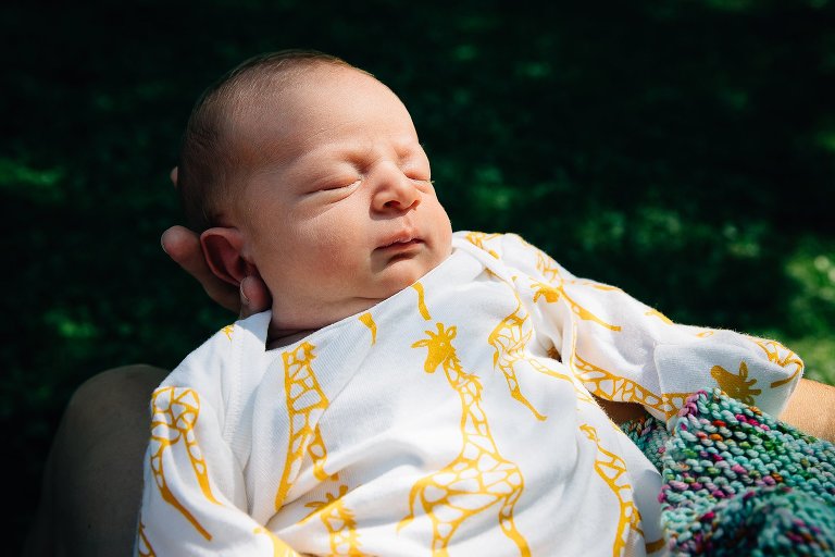 Sleeping newborn baby held outside with the sun shining on his face.