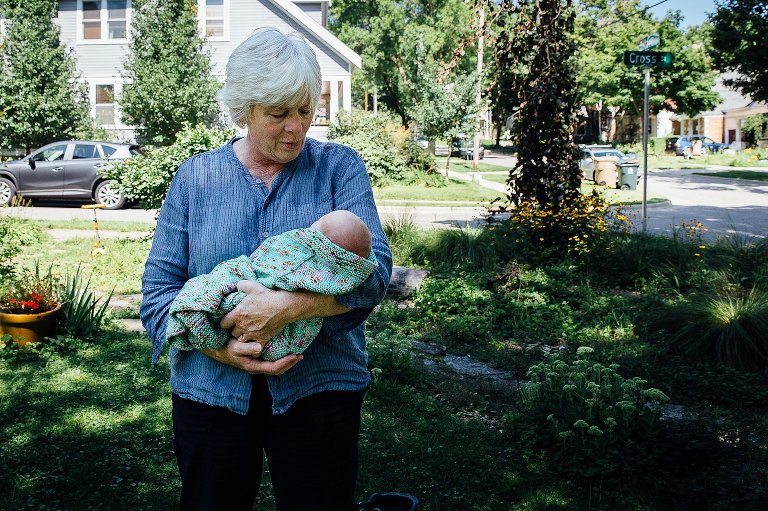 Grandma holds sleeping newborn baby in front yard.
