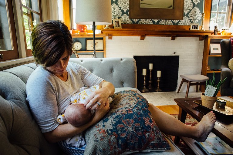 Mother sits on couch while nursing newborn baby.