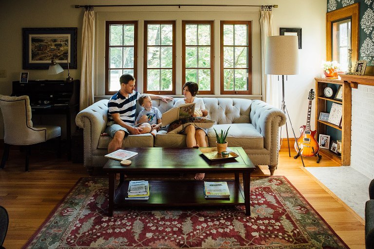 Family sitting on a couch in the living room read a story together. 