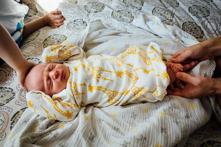 Newborn baby wearing a yellow giraffe onesie sleeps on a bed.