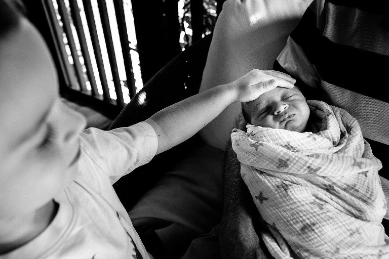 Black and white. Older brother strokes sleeping baby's head.