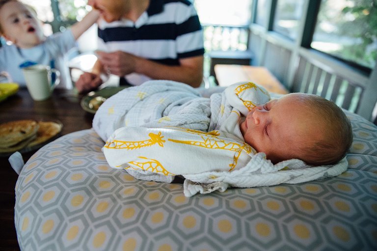 Swaddled newborn baby sleeps as family eats chocolate chip pancakes for breakfast.