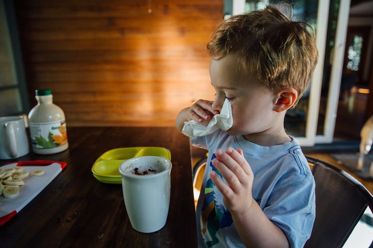 Young boy wipes his mouth with a napkin as he eats breakfast on back porch.