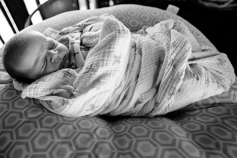 Black and white. Newborn baby in swaddle blanket sleeping on a cushion.