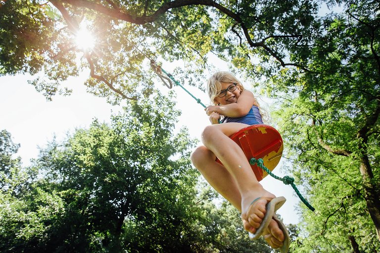 Young girl swinging on a swing hanging from big tree in her backyard.
