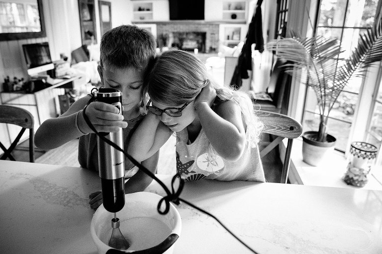 Black and white. Brother and sister use a electric whisk to mix pancake batter for breakfast.