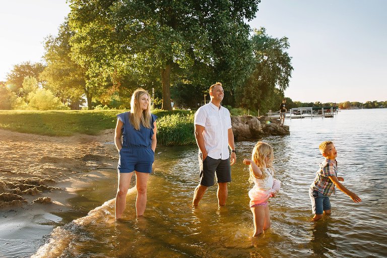 Family of four standing at the beach with their feet in the water. Sun setting behind them casting a golden color.