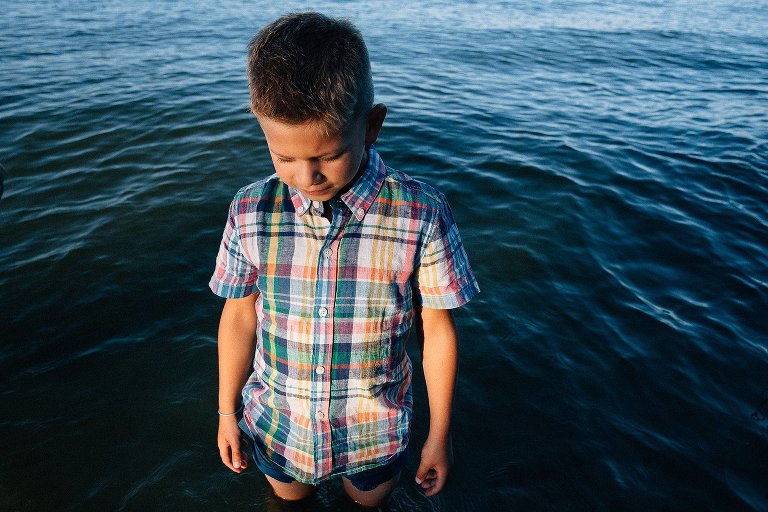 Young boy standing with his feet in the lake.