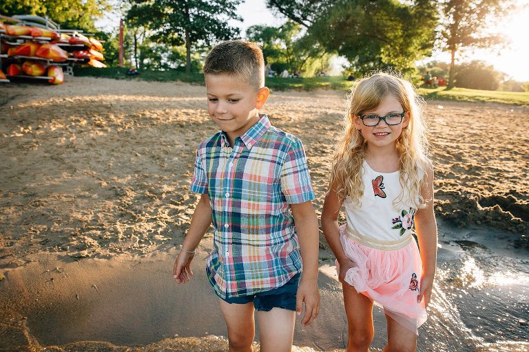 Brother and sisters stand at the edge of the beach with their feet in the water.