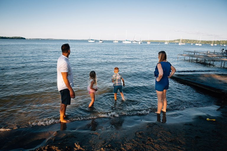 Mom and dad stand at the beach while their kids play in the water.