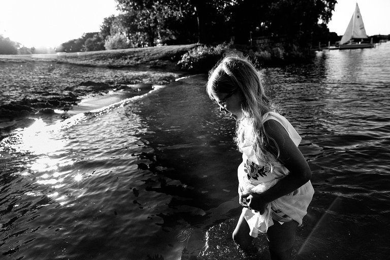 Black and white. Young girl runs around in the water holding up her dress.