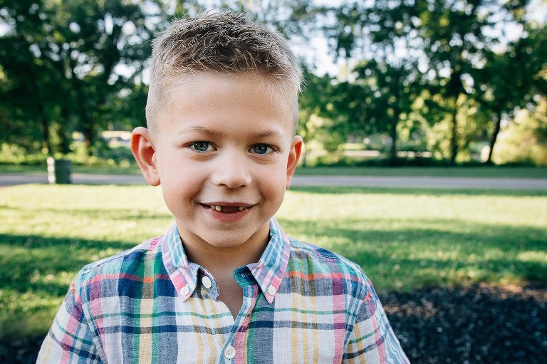 Young boy standing at a park smiles missing his two front teeth.