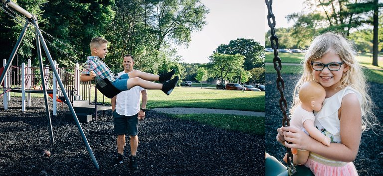 Father watching his son swing on a swings at a park. Young girl with long curly blonde hair holds a baby doll.