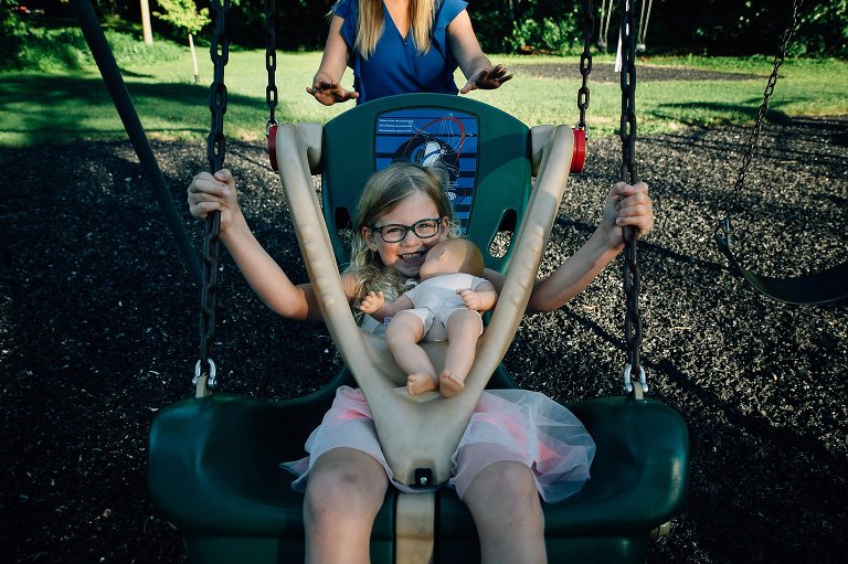 Mom pushes her daughter in the swing at a park.
