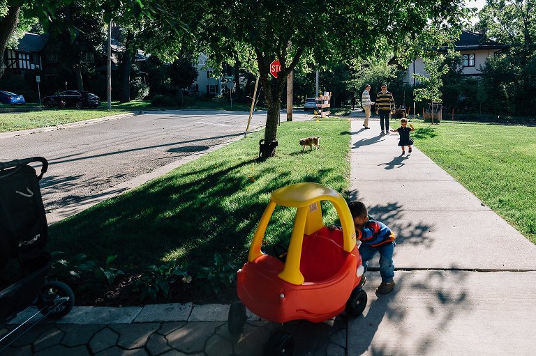 Color. Family of four and 2 dogs play on the front lawn. 