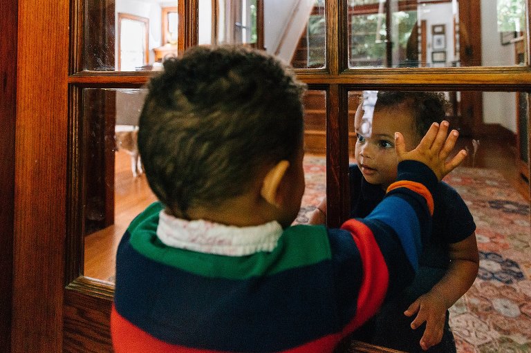 Two toddlers look at each other between a glass door.